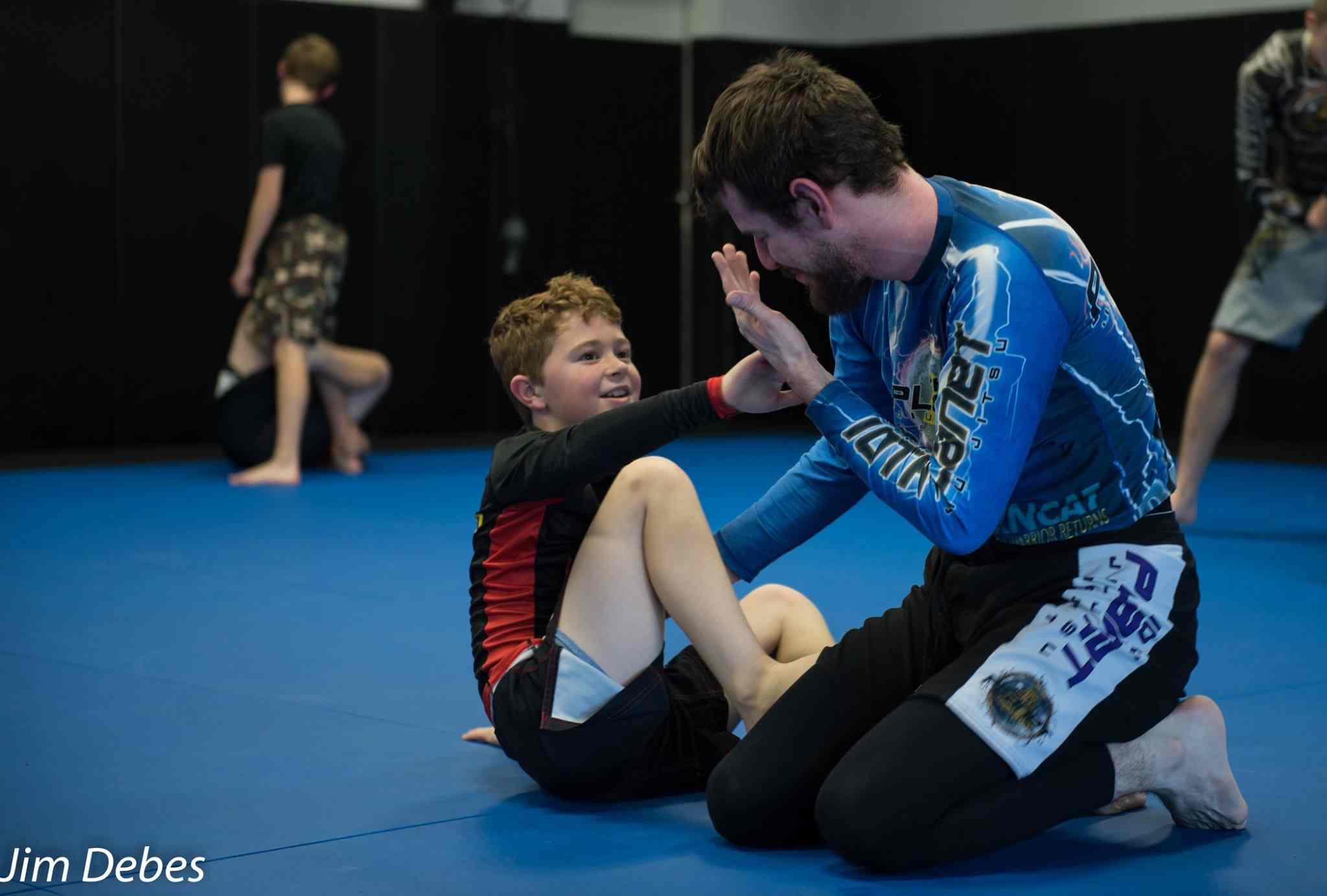 A Caucasion adult male teaching a young, Caucasion male student jiu-jitsu.