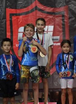 Young, smiling kids wearing 10th Planet Beaumont shirts and shorts and 1st place jiu-jitsu competition medals.